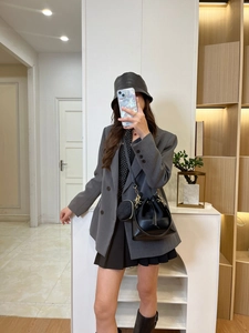 Close-up of a stylish black drawstring bucket bag with a small round charm on a gray blazer