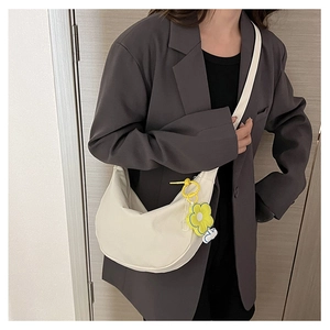 Gros plan du sac hobo minimaliste crème avec breloque tournesol sur un blazer gris
