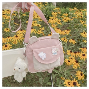 Detail of pink cartoon crossbody bag with cute ear design and plush bear charm outdoors