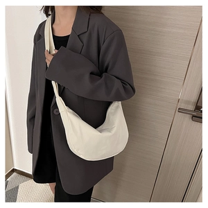 Détail d'un sac bandoulière demi-lune crème porté sur un blazer gris foncé