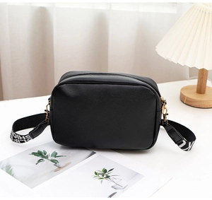 Detail of black V-pattern PU leather crossbody bag with wide white letter printed strap