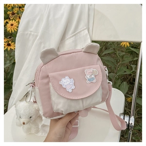 Close-up of pink and white cartoon bear crossbody bag with cute plush charm on a chair