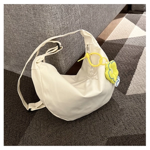 Détail du sac bandoulière demi-lune blanc crème avec charm fleur jaune sur un canapé