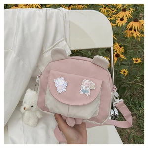 Close-up of pink and cream crossbody bag with bunny ears and plush bear on a white chair
