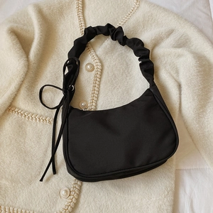 Schwarze Retro-Hobo-Tasche mit plissiertem Trageriemen und Schleife auf Strick-Hintergrund