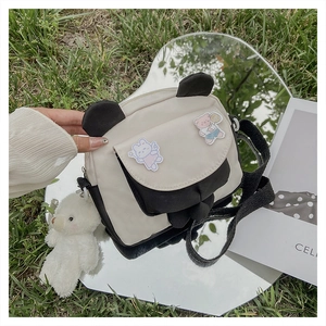 Detail of panda style crossbody bag with cute pins and plush bear charm on grass