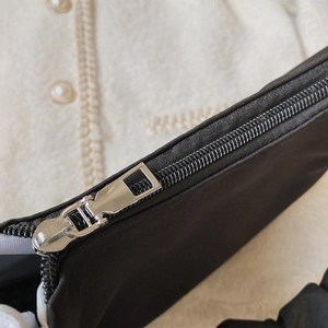 Detailansicht des silbernen Metallreißverschlusses und des schwarzen Faltenstoffs der Tasche