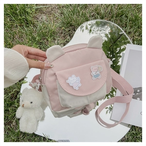 Close-up of pink and cream crossbody bag with a plush bear charm on outdoor grass