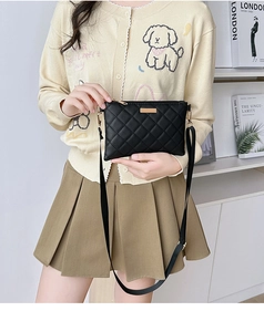 Close-up of black quilted shoulder bag with gold metal plate on a beige cardigan outfit