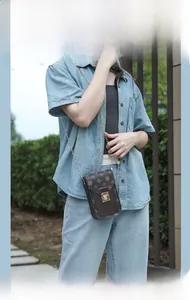 Detailed view of monogram brown crossbody phone bag with gold chain strap on denim outfit