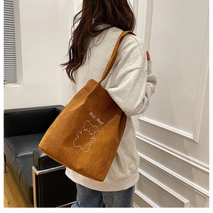Borsa tote in velluto a coste marrone con ricamo di orso indossata da modella casual