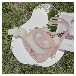 Pink and white canvas crossbody bag with cartoon bear patch on outdoor mirror surface
