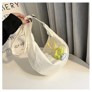 Détail du sac demi-lune en toile blanche avec breloques florales et bandoulière réglable