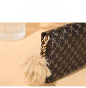 Macro view of gold zipper and large khaki faux fur pompom on brown leather wallet