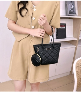 Detail of black quilted tote bag with golden logo and small round charm pendant