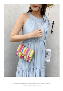 Close-up of a colorful woven rainbow straw bag with golden chain strap on a model