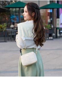 Detail of cream quilted crossbody bag with gold metal trim and patterned wide strap