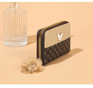 Detail of zip wallet with floral print, gold butterfly hardware and plush ball charm