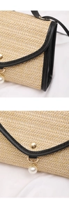 Detail of woven straw bag featuring black leather trim and elegant pearl pendant accent