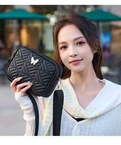 Close-up of black quilted crossbody bag with silver butterfly charm and wide strap