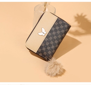 Detail of compact zip wallet featuring butterfly metal accent and plush fur pompom charm