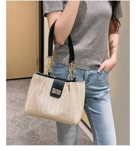Detail of straw bucket bag featuring golden chain strap and leather accents on model