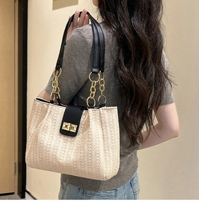 Close-up of woven tote bag with black leather flap and gold metal turn-lock buckle