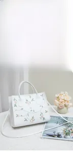 Detail view of floral embroidery on a white crossbody tote bag with adjustable strap