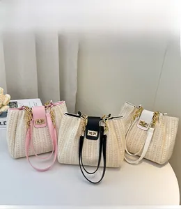Three woven straw tote bags in pink, black, and white with metal chain straps on a table