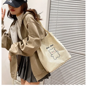 Modella che indossa una borsa tote in velluto a coste crema con ricamo di orso