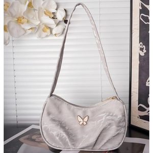 Detail of grey pleated shoulder bag featuring a golden butterfly metal ornament