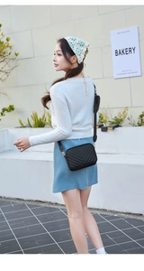 Close-up of black V-quilted crossbody camera bag with wide strap and coin purse detail