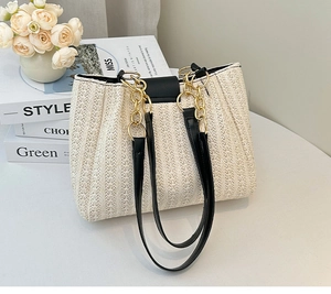 Close-up of woven straw tote bag with black leather straps and gold chain link details