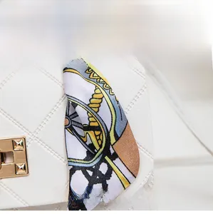 Detail of white quilted crossbody bag featuring golden turn-lock and vintage silk scarf