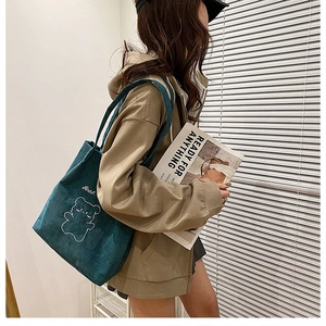 Dettaglio di borsa tote in velluto a coste verde scuro con ricamo a orsetto
