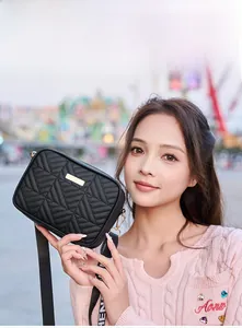 Detail of black quilted camera bag with gold metal plate and wide woven strap