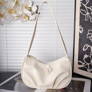 Detail of cream pleated baguette bag with butterfly ornament and top zipper closure