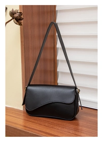 Détail du sac bandoulière noir en cuir avec un rabat à coupe ondulée élégante