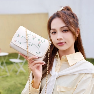 Elegant white chain crossbody bag with sweet floral embroidery on natural grass background