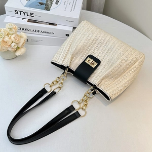 Straw shoulder bucket bag with black leather trim and gold chain strap on white desk