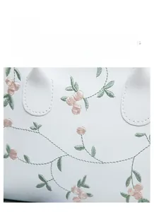 Close-up of white leather handbag with floral embroidery and lychee grain texture