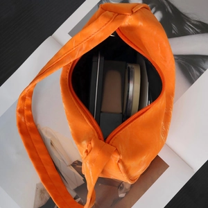 Internal storage view of an orange pleated underarm bag showing makeup essentials