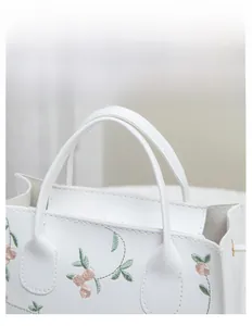 Detail of white leather handbag with floral embroidery and reinforced handles