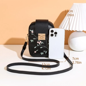 Detail of floral embroidery and gold metal buckle on a black vertical shoulder bag