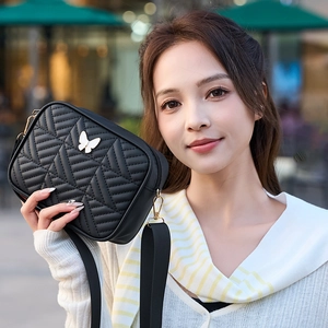 Elegant black quilted crossbody bag with white butterfly motif and wide strap on street