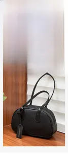 Close-up of black lychee grain leather bowling bag with dual handles and fashion tag