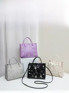 Detail of four embroidered mini tote bags in purple, grey, black, and beige colors