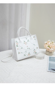 Detail of white embroidered tote bag with pink floral patterns and long shoulder strap