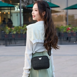 Quilted crossbody camera bag with silver butterfly charm worn by a model in city street
