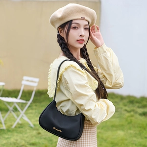 Lychee texture black underarm bag with gold logo shown on a model in a natural setting